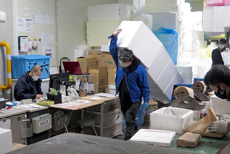包装資材が山積みの東京魚類容器6街区売場の一角で伝票整理する原社長（左）